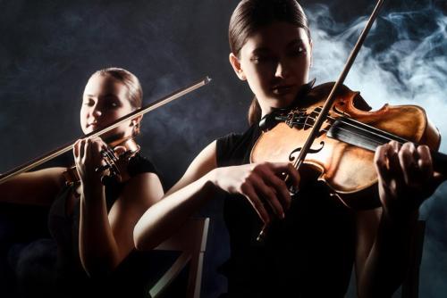 beautiful musicians playing on violins on dark stage with smoke